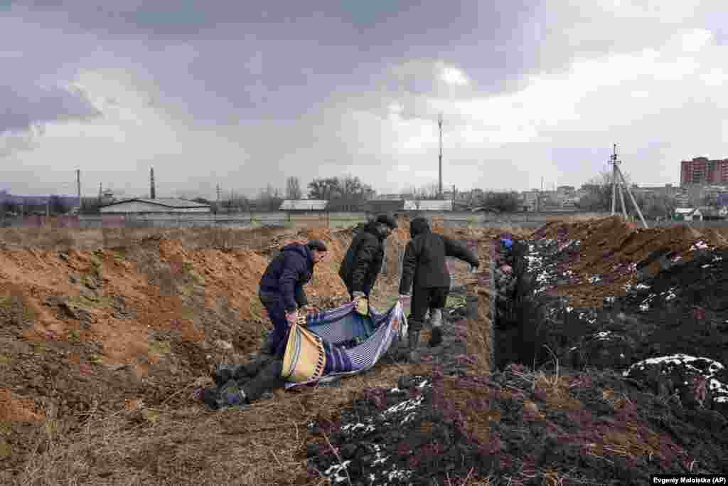 Tres individuos arrastran cadáveres a ser depositados en una larga fosa común en las afueras de Mariúpol, el 9 de marzo.