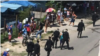 Boinas negras caminan junto a personas que permanecen en una cola.